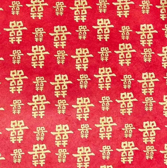 Red paper with a repeating pattern of gold Chinese double happiness symbols.
