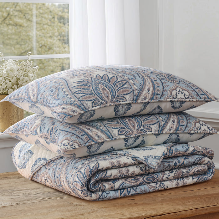 Folded paisley-patterned comforter on a wooden surface with a window in the background