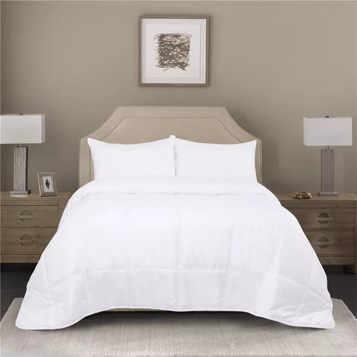 White quilted comforter on beige upholstered bed frame with matching nightstands and lamps