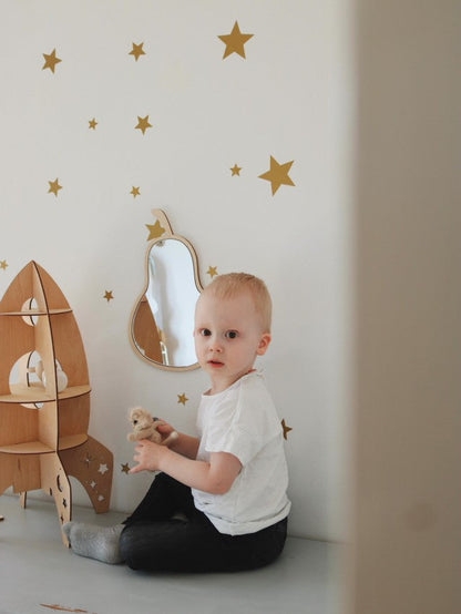 Child sitting beside pear mirror wall hanging in bright nursery with star wall decorations