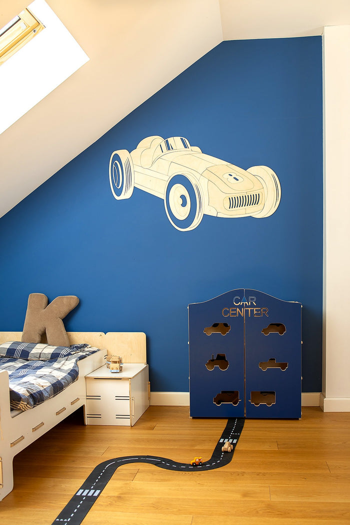 Wooden formula one car decal on blue wall next to white nightstand and toy garage