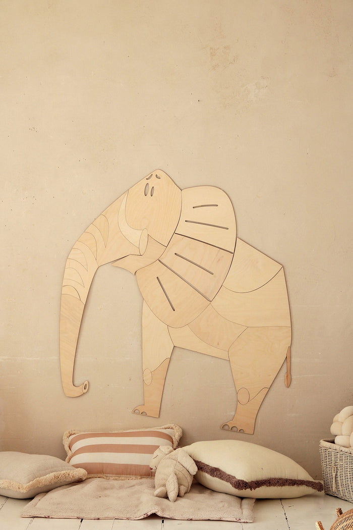 Wooden elephant wall decoration mounted on beige wall above cushions and toys in nursery