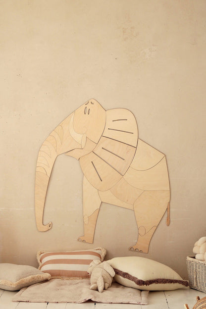 Wooden elephant wall decoration mounted on beige wall above cushions and toys in nursery