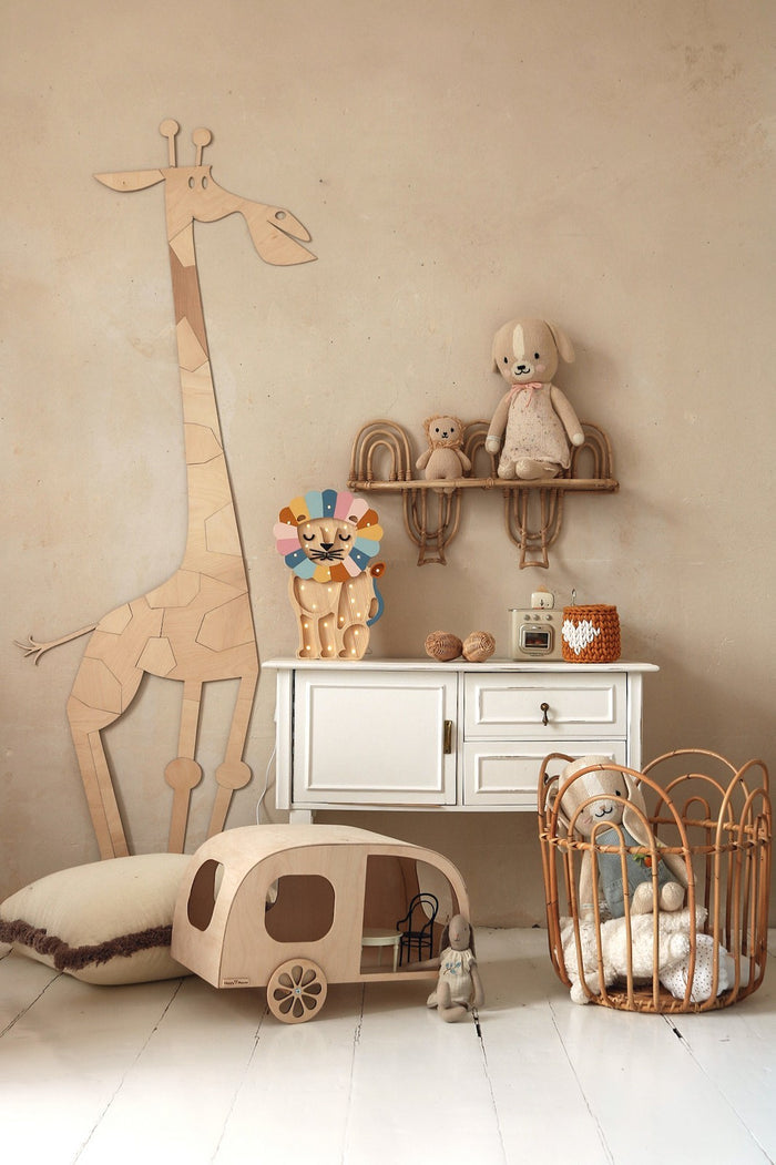 Natural wood giraffe wall decoration beside white dresser with shelves holding toys and nursery accessories