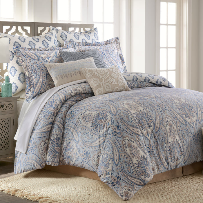 Bed with paisley patterned bedding and pillows in a bright room.