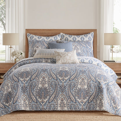 Blue and white patterned comforter set on a bed in a bedroom with lamps and decor.