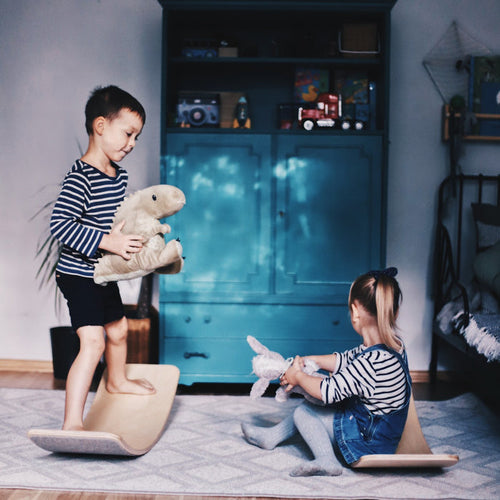 Two children balancing on wooden balance boards with grey felt, playing together indoors