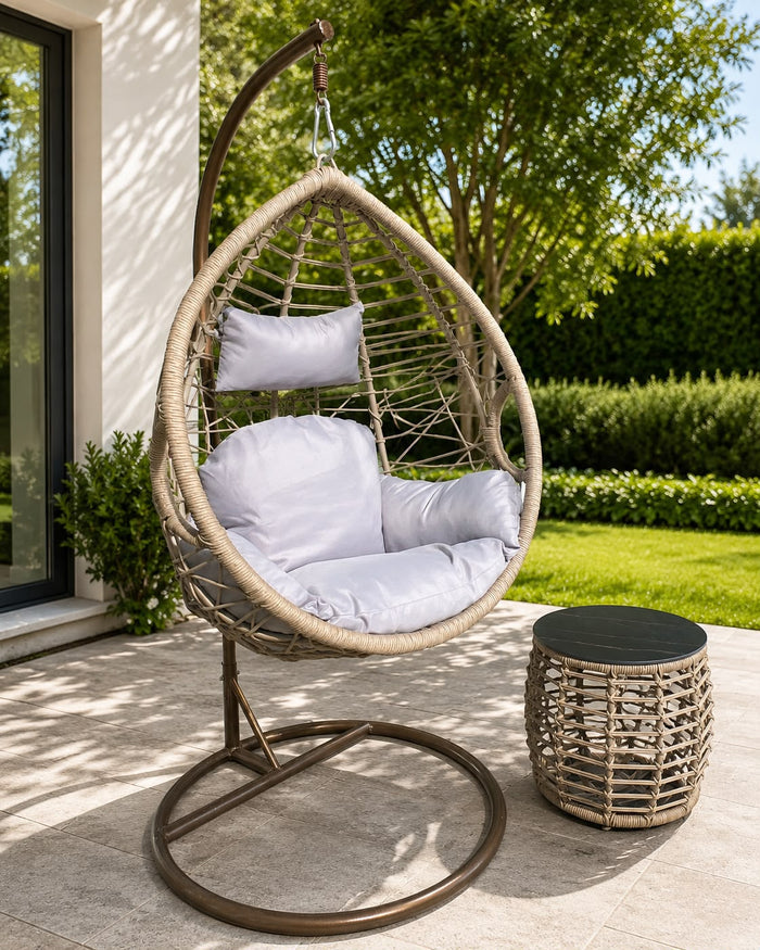 Rattan hanging egg chair with white cushions and side table on patio