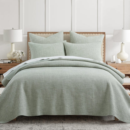 Green checkered quilt and pillow set on a bed in a bedroom setting.