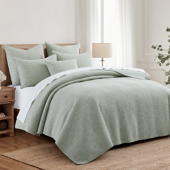 Bed with green bedding and pillows in a bedroom setting