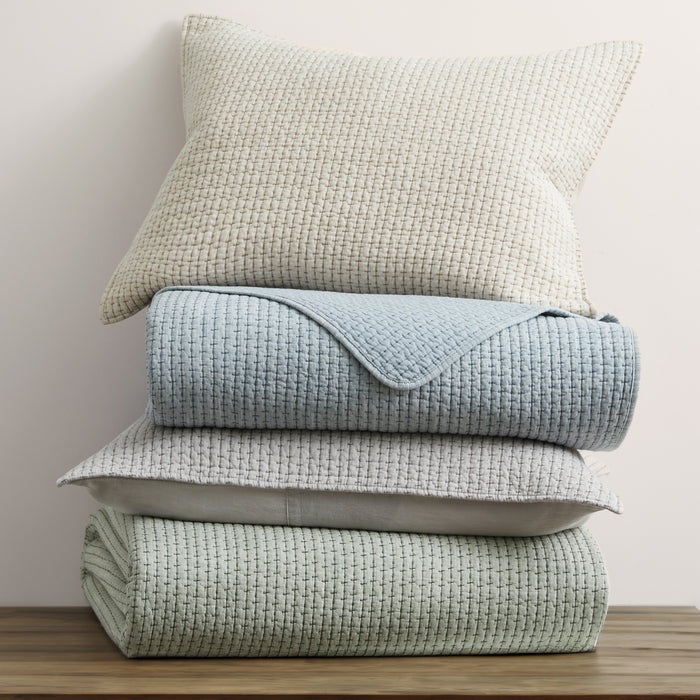 Stack of textured light blue and green blankets with a pillow on a wooden surface.
