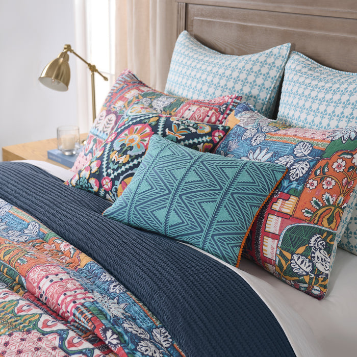 Roshita Quilt Set displayed on a bed featuring vibrant patchwork design and decorative pillows in a cozy bedroom setting.