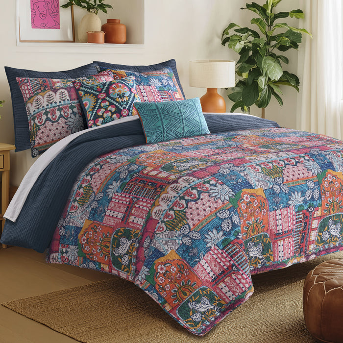 Roshita Quilt Set featuring vibrant patchwork design on a bed with blue accents and decorative pillows.