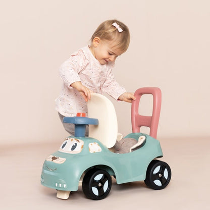 Toddler sitting on turquoise ride-on pusher with pink handle and horn, demonstrating seated play
