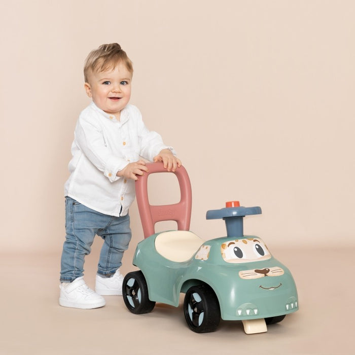Child standing beside turquoise ride-on pusher holding pink backrest handle