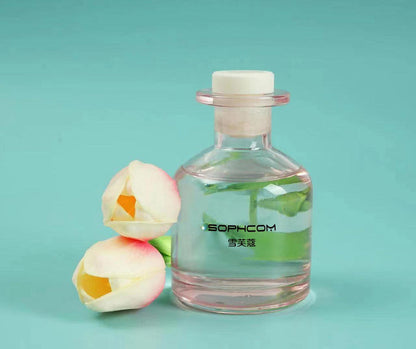 Glass fragrance diffuser bottle with floral stems and two artificial white tulip flowers on a teal background